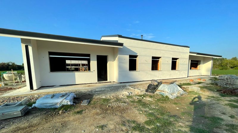 Edificio residenziale a un piano con copertura piana e intonaco chiaro, in fase di finitura, con area di cantiere in primo piano.
