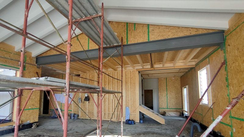 Interno di edificio in costruzione con telaio portante in legno, pannelli OSB, travetti di solaio e trave in acciaio, con ponteggi in primo piano.
